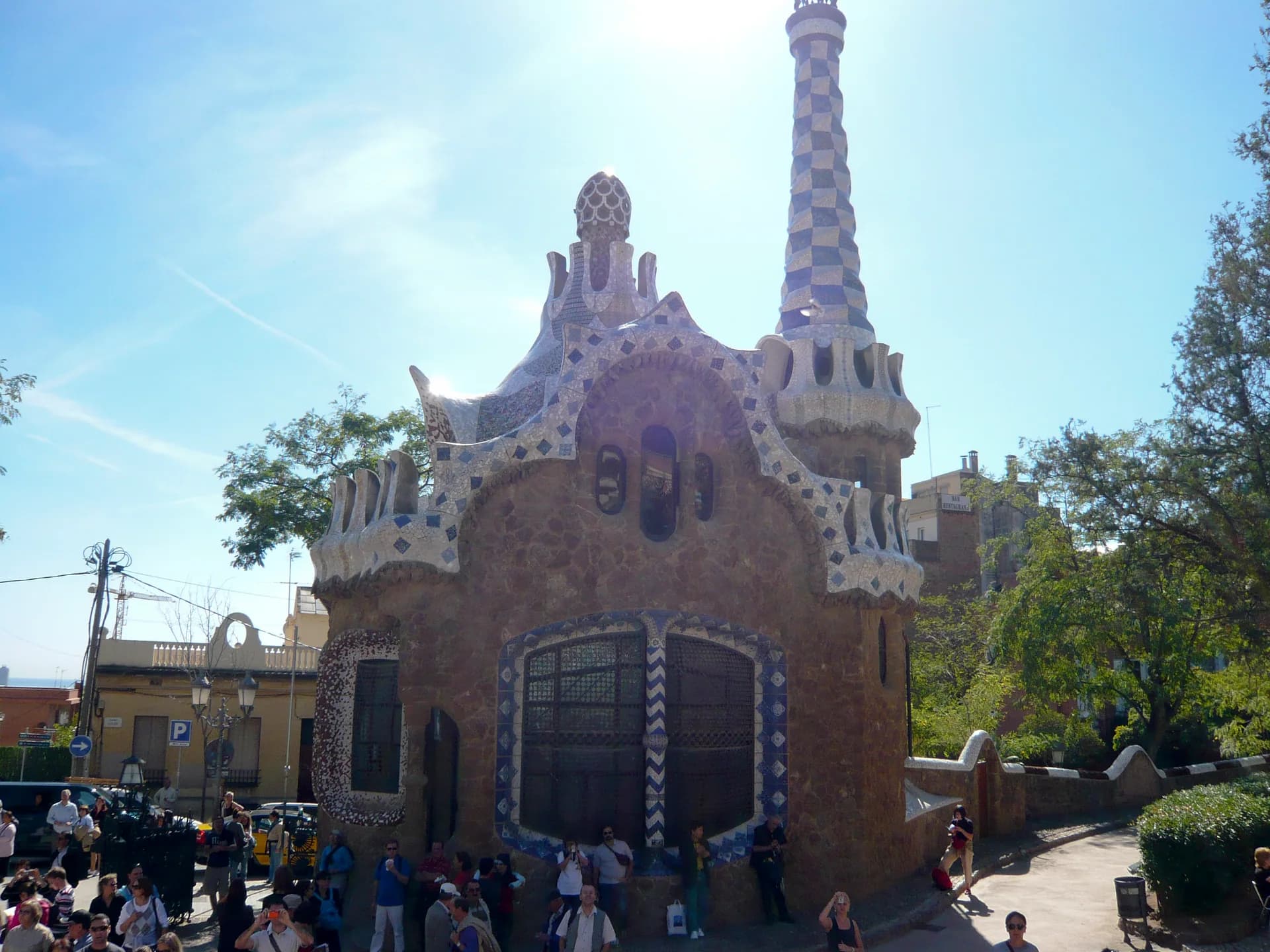 El pavelló d'entrada del Park Güell, amb la torre de trencadís, i visitants a la plaça