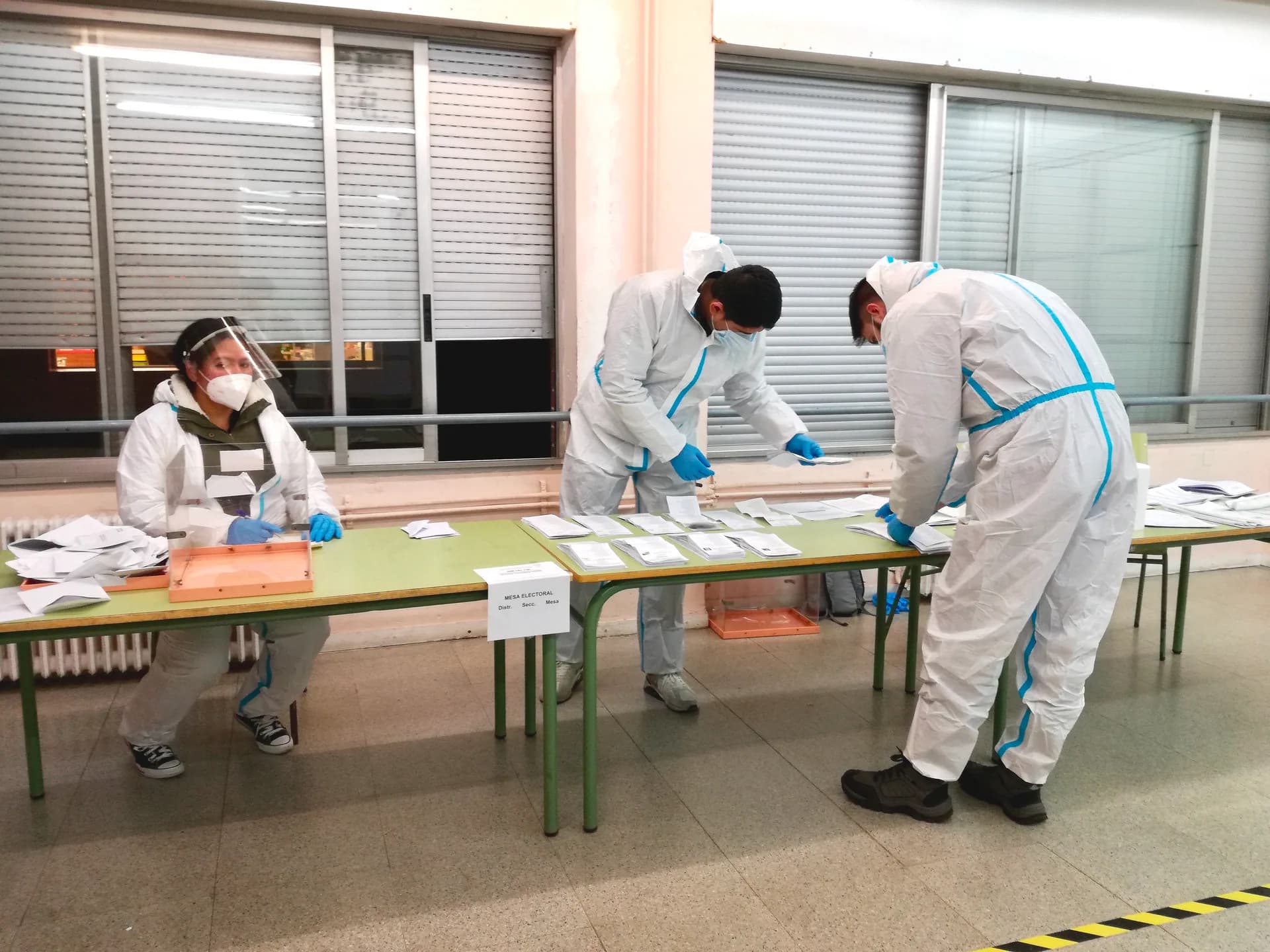 Tres persones amb equips de protecció ordenant paperetes sobre unes taules