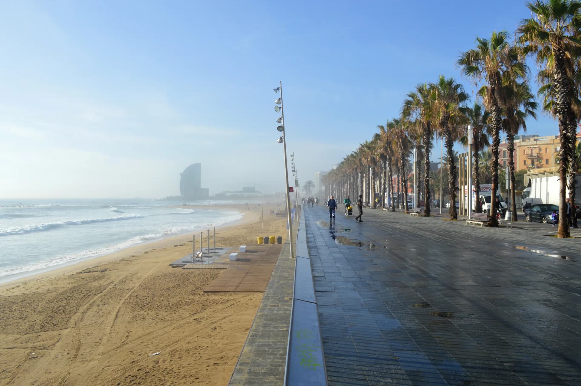 La playa de la Barceloneta y el paseo marítimo con palmeras, con el hotel W al fondo