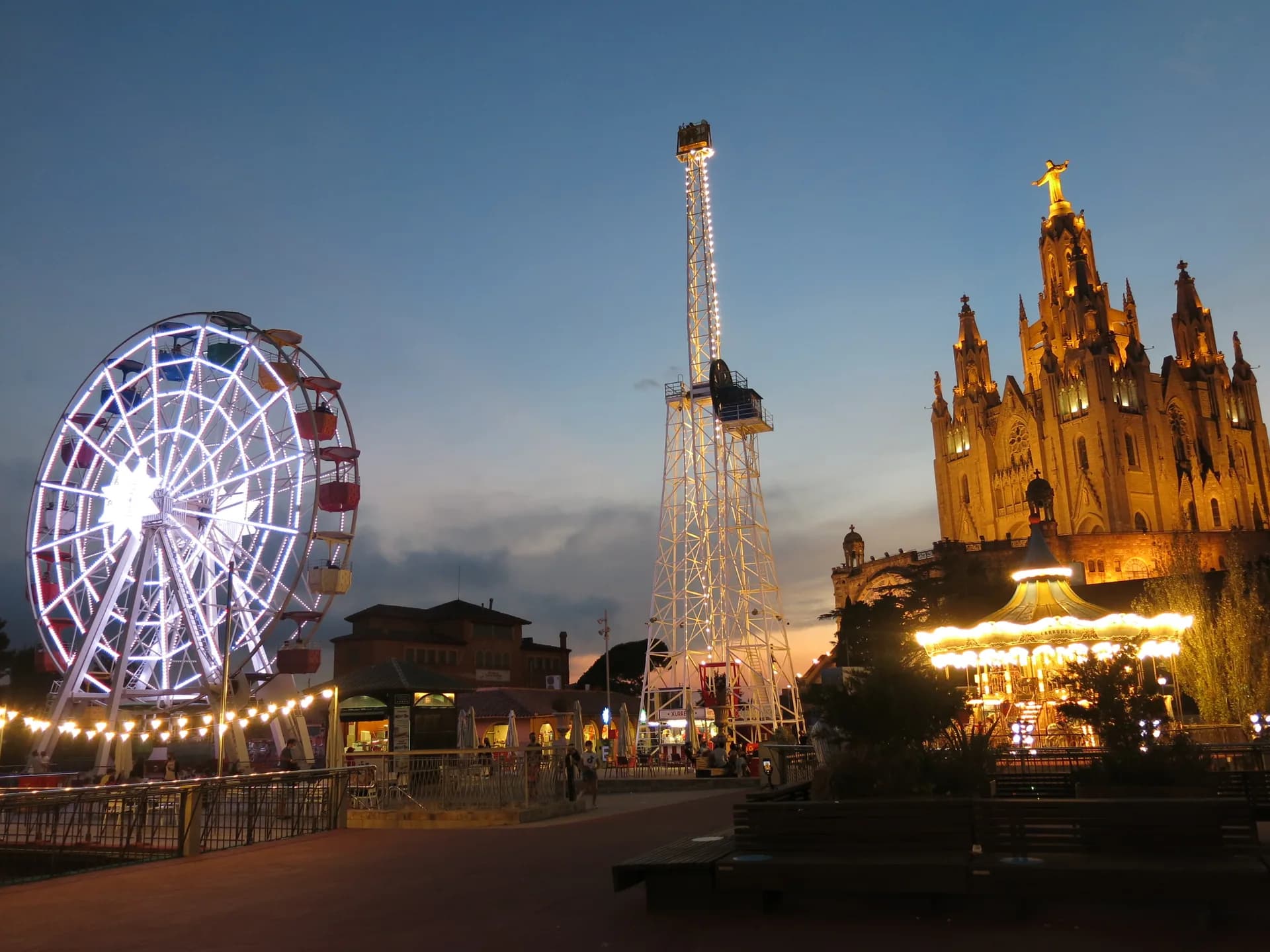 La sínia i les atraccions del Tibidabo il·luminades al capvespre, amb el Sagrat Cor al fons